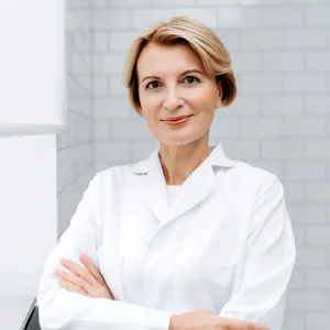 Dentist near me in Sacramento wearing a white coat with arms crossed in a bright, modern dental clinic